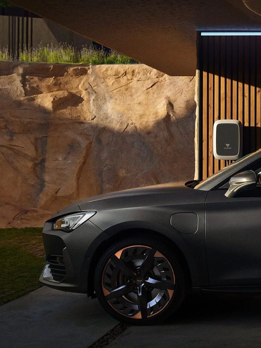 Moški stoji ob parkiranem temnosivem avtomobilu v sodobni garaži. V roki drži mobilni telefon. 