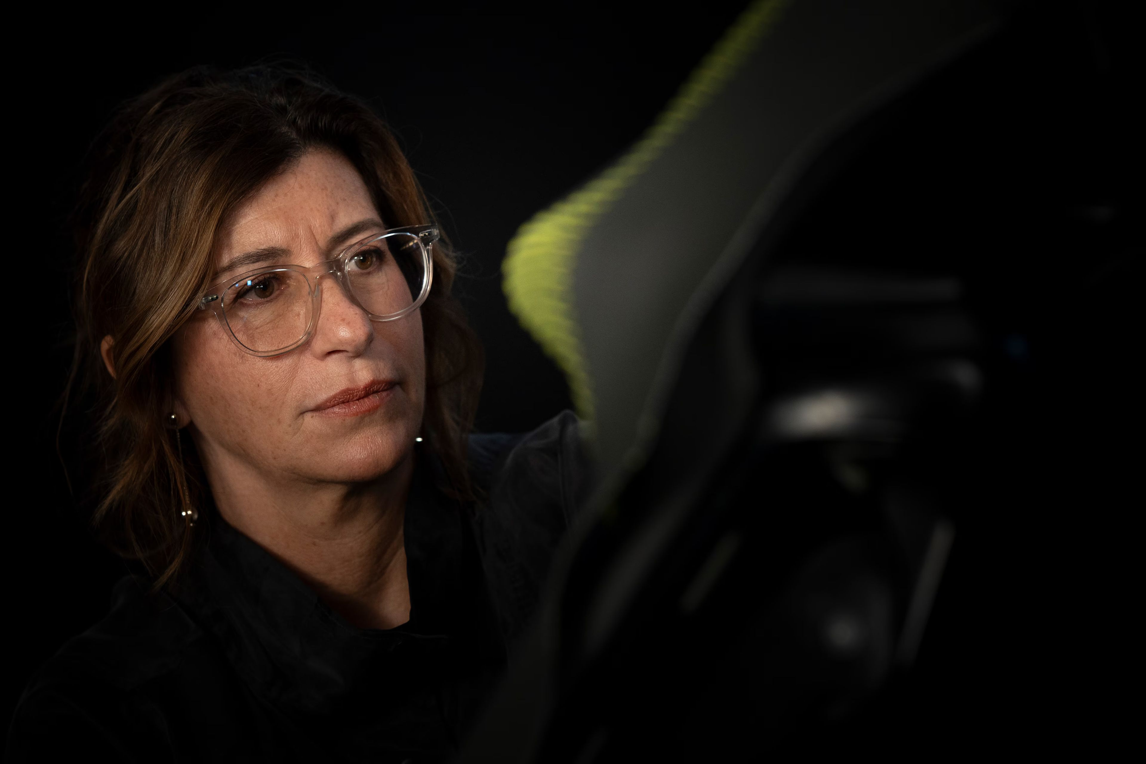 Ženska z očali pozorno pregleduje material. Prizor poudarja natančnost, osredotočenost in proces razvoja izdelka.