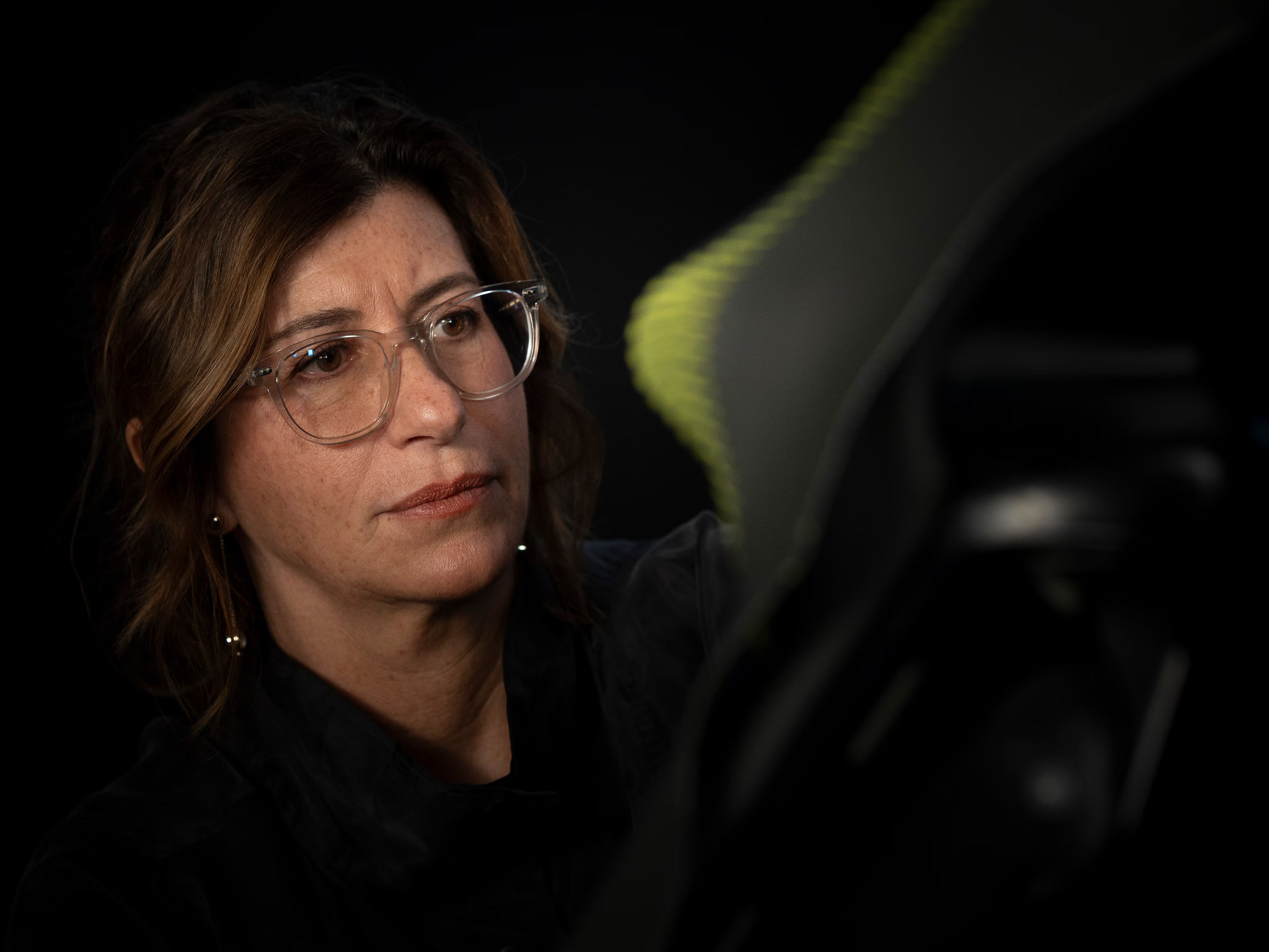 Ženska z očali pozorno pregleduje material. Prizor poudarja natančnost, osredotočenost in proces razvoja izdelka.