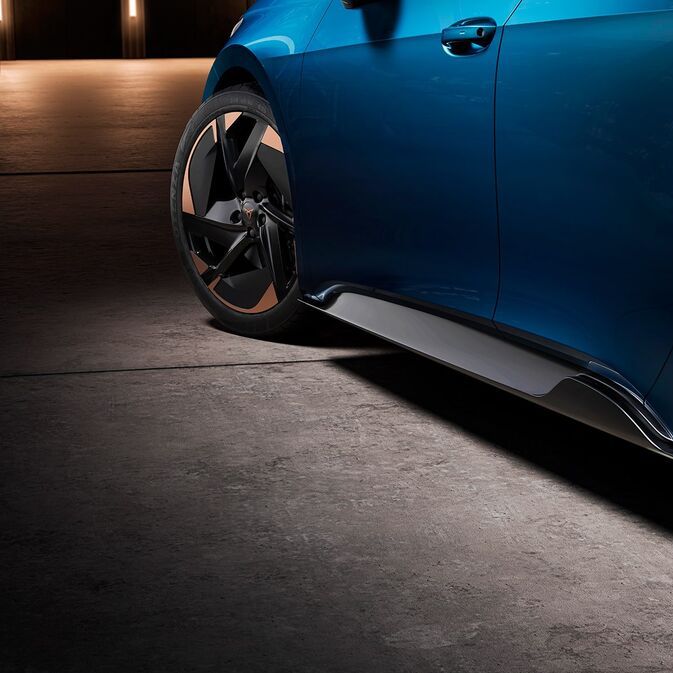 Parkiran modrega avtomobila Cupra Born z dvema vidnima kolesoma na betonskem vozišču. Pnevmatike avtomobila imajo temne platišča z bronastimi detajli.