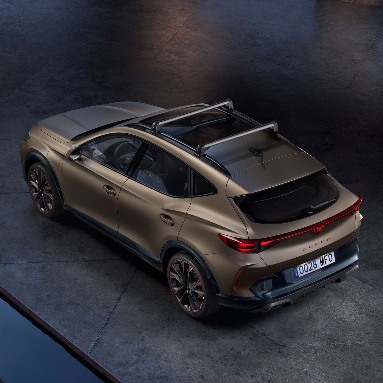 SUV Cupra Formentor avto v bronasti barvi je parkiran na betonski površini. Na strehi ima pritrjene strešne nosilce.