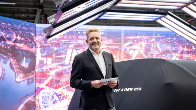 Wayne Griffiths stoji na odru. Za njim je velik digitalni zaslon, ki prikazuje mesto ponoči. Poleg njega je velik avtomobil znamke CUPRA, prekrit s črnim blagom.