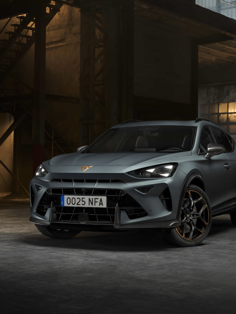 Športni terenec CUPRA Formentor stoji v industrijskem skladišču z zatemnjenimi lučmi. Avto je obarvan v sivo mat barvo in črno-zlate platišča. V ozadju so vidni veliki okni, ki delno osvetljujeta prostor.