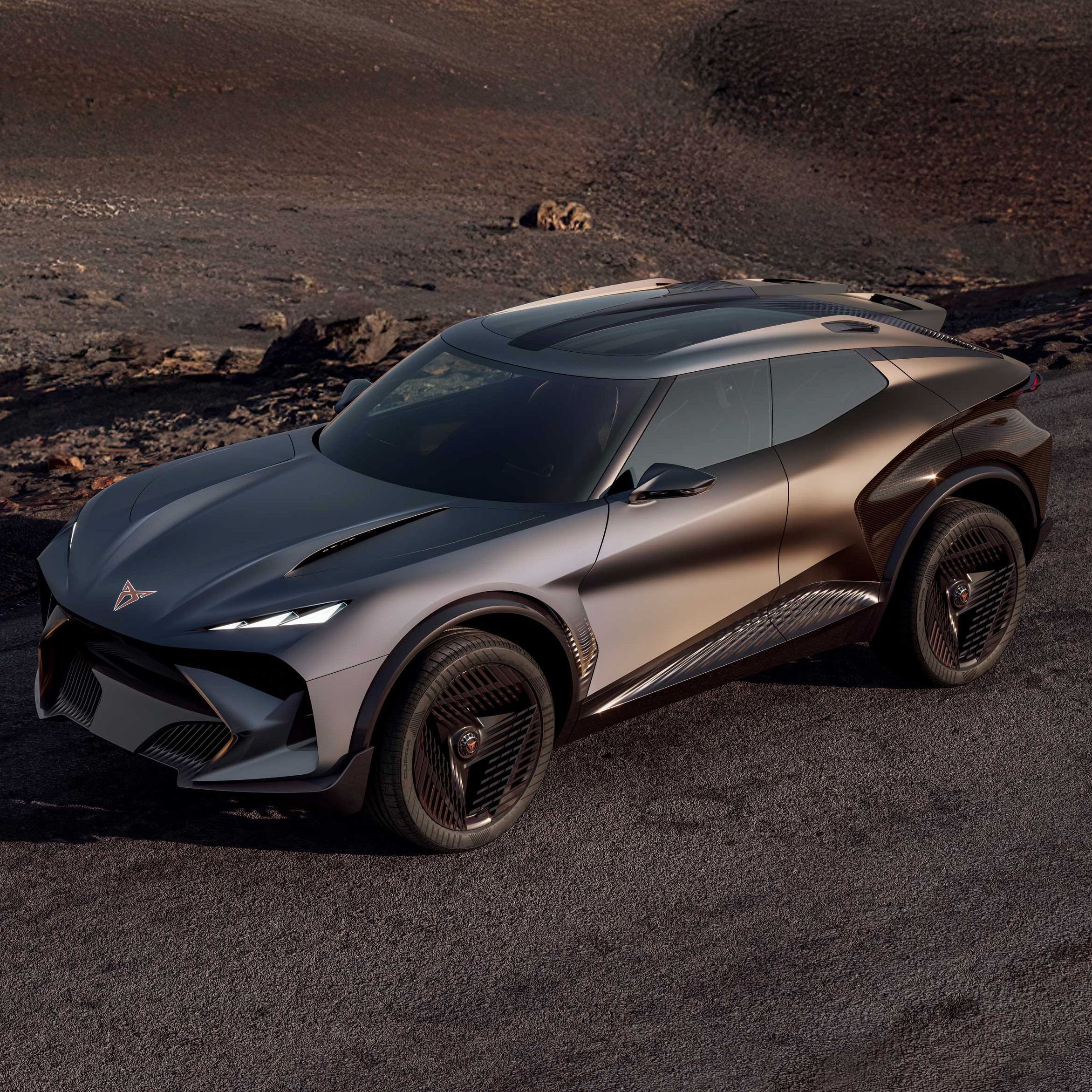 Futurističen športni SUV s kovinsko sivo karoserijo z ostrimi linijami in velikimi črnimi platišči vozi po prazni, asfaltirani cesti. V ozadju je surova, kamnita, skoraj vulkanska pokrajina brez vegetacije. Avto deluje kot konceptno vozilo z agresivnim dizajnom in poudarjenimi aerodinamičnimi elementi.