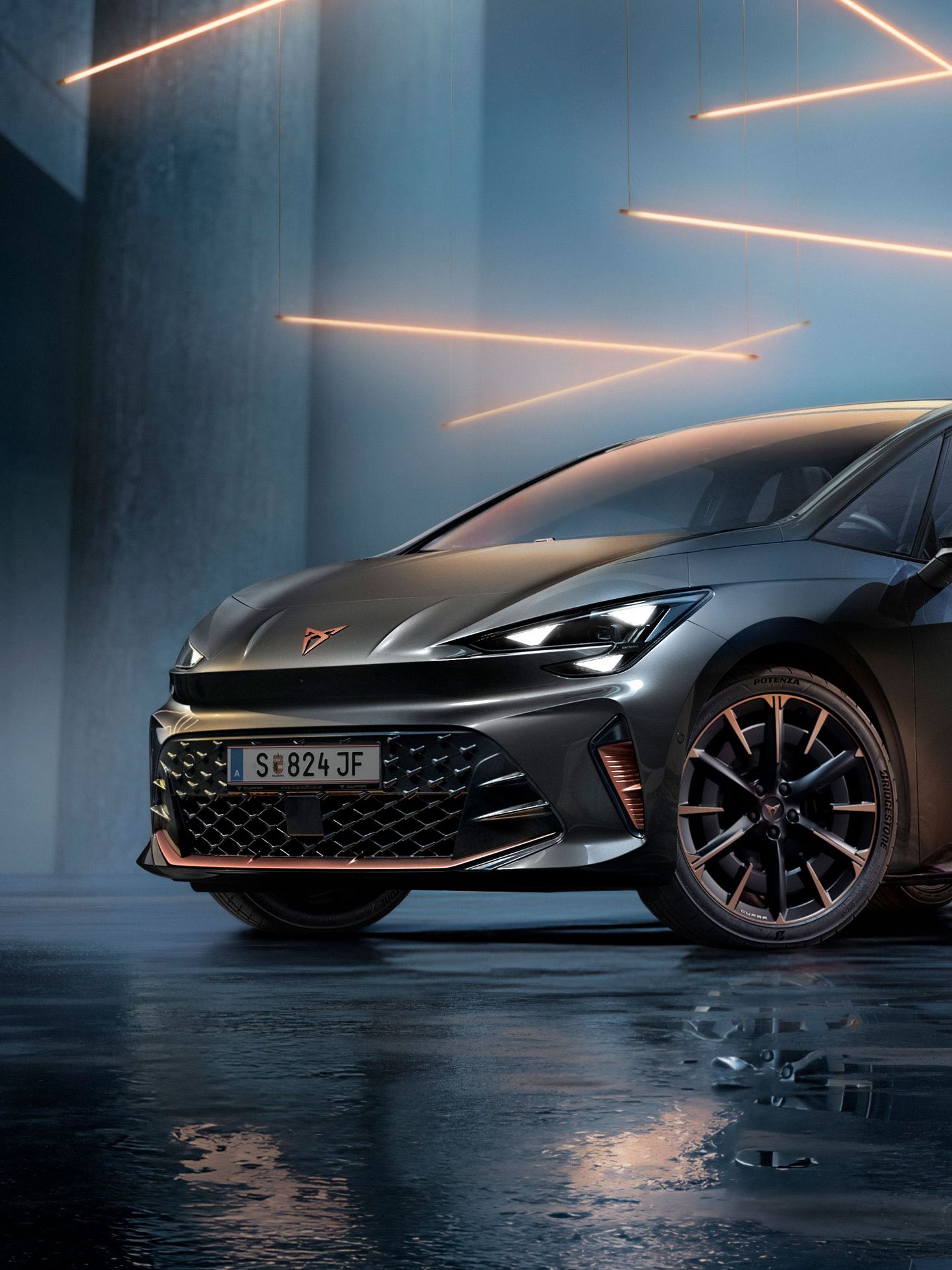 Ein grauer CUPRA Born steht in einer modernen, dunklen Umgebung mit vertikalen Säulen und leuchtenden LED-Streifen. Der Boden ist glänzend und reflektiert das Fahrzeug sowie die Beleuchtung. Das Auto wirkt kraftvoll und elegant.