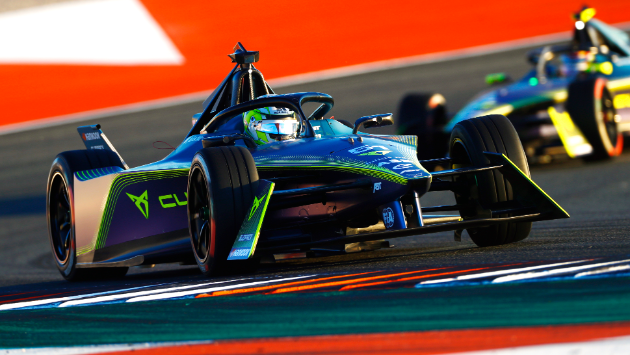 Dva dirkalnika znamke CUPRA formule E tekmujeta na stezi med dirko. Vodilni dirkalnik je temno modro-zelen, drugi pa je v ozadju.